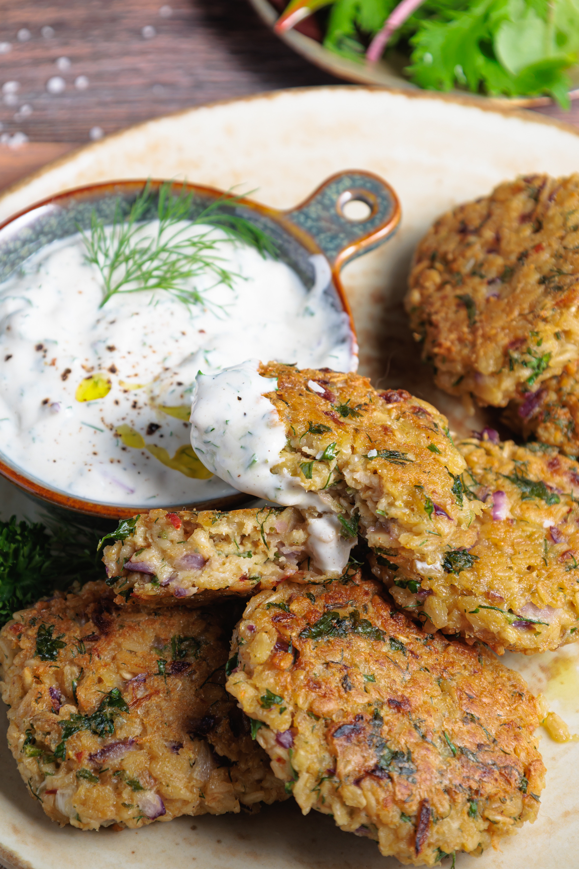 Haferflocken-Frikadellen auf einem beigen Teller, daneben ein veganer Joghurt-Kräuter-Dip in einem Schälchen
