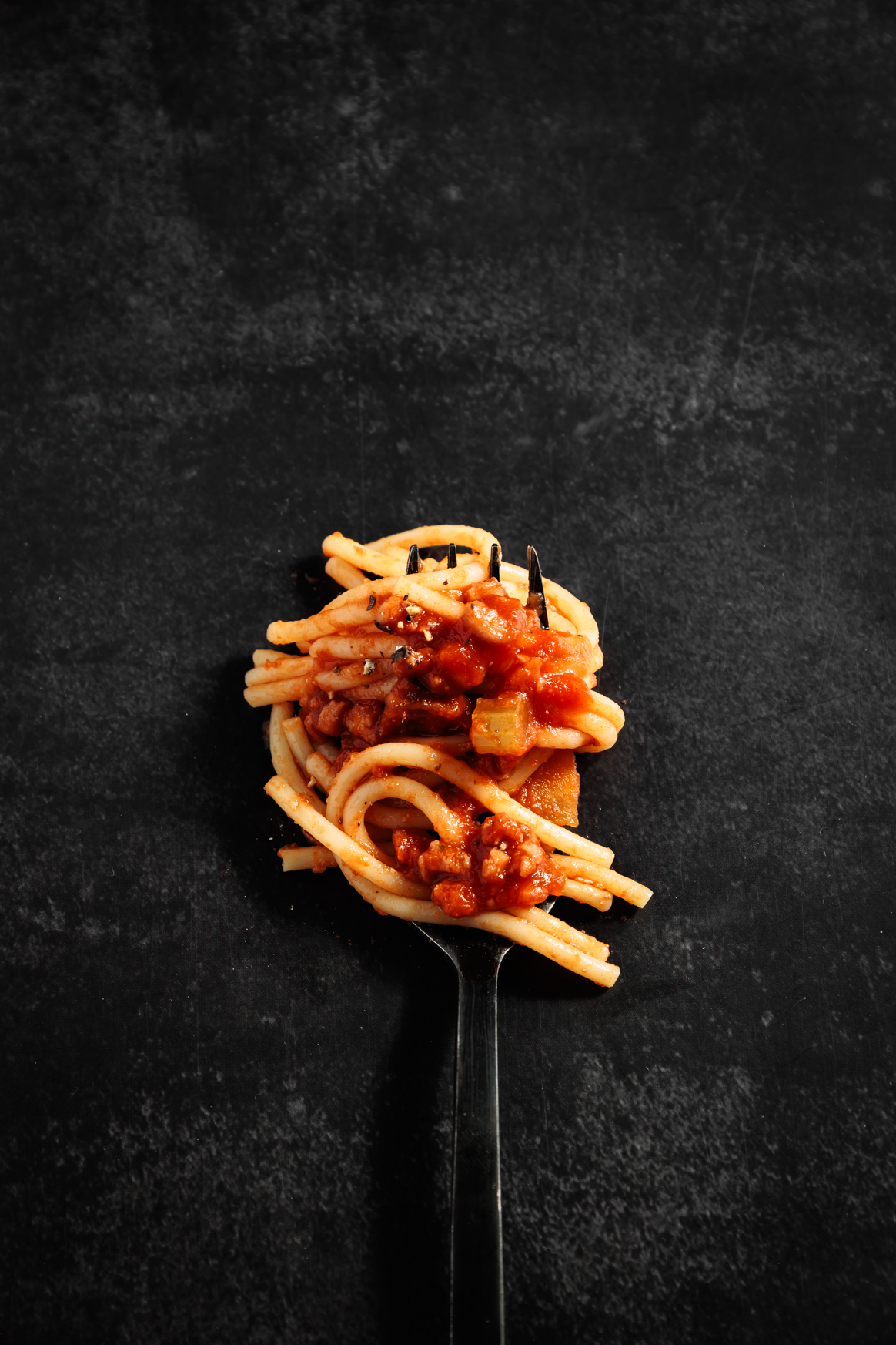 Spaghetti Bolognese auf einer Gabel auf dunklem Untergrund.